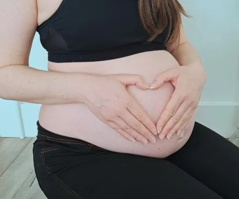 Chéile Wellbeing pregnancy mental health support: a pregnant woman making a heart shape with her hands over her bump